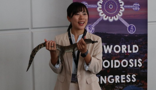 Delegate holding crocodile in front of conference banner
