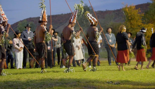 Anangu cultural welcome on lawns in front of mountain range in Alice Springs