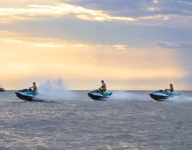3 jet skis on the ocean during sunset 