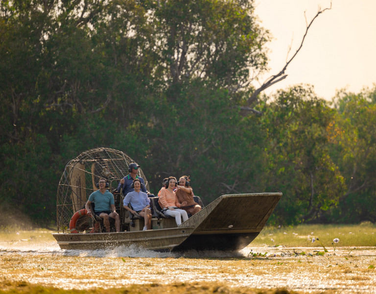 A group enjoys an airboat tour through a lush wetland, smiling as they ride across the water.