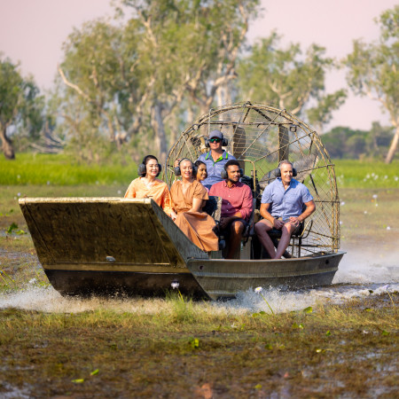 A group enjoys an airboat tour through a lush wetland, smiling as they ride across the water.