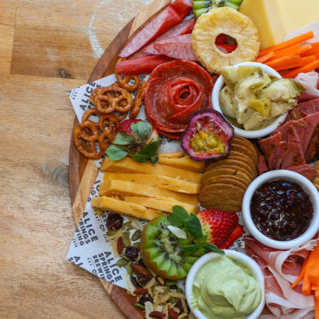 A large grazing platter featuring cheeses, meats, crackers, fresh fruit and dips arranged on a wooden board.