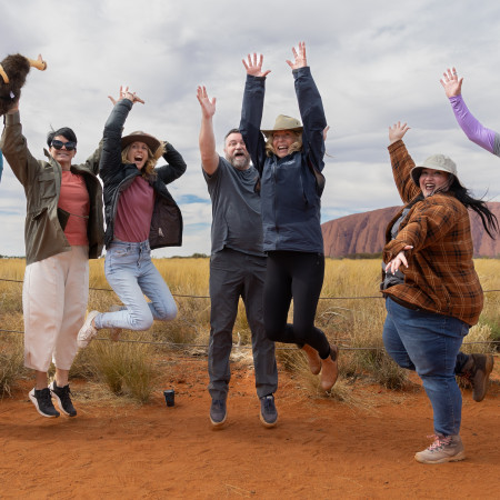 group of people jumping in front of Uluru
