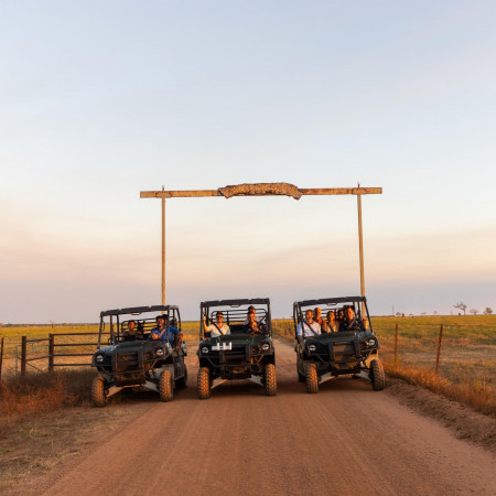 Three off-road tour vehicles parked beneath the Finniss River Lodge entrance sign on a dirt road.