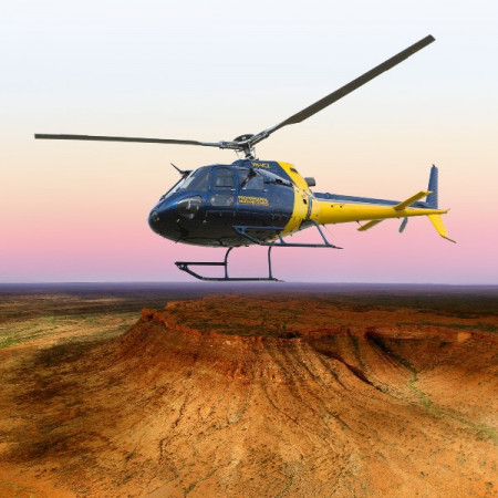 Helicopter hovering above red desert ridge at sunset in Central Australia.