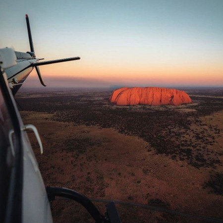 View of Uluru at sunset seen from inside a helicopter over Central Australian desert.