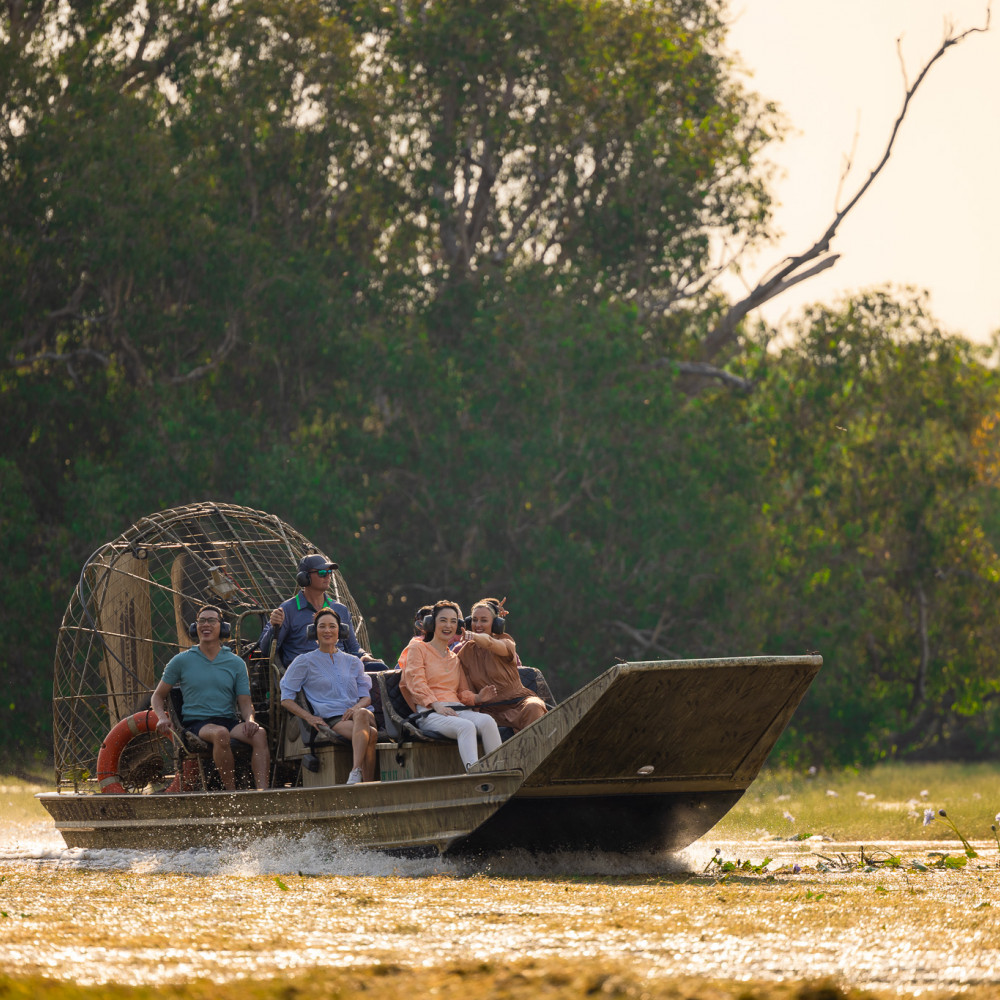 A group enjoys an airboat tour through a lush wetland, smiling as they ride across the water.