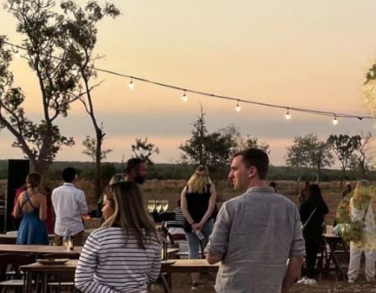 Group of people in outdoor setting with tables, fairy lights and trees