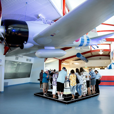 People gathered under plane wing at Royal Flying Doctor Service Tourist Facility