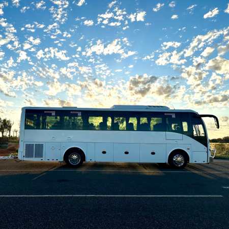 Background of clouds and blue sky with a Tour Bus driving through the NT 
